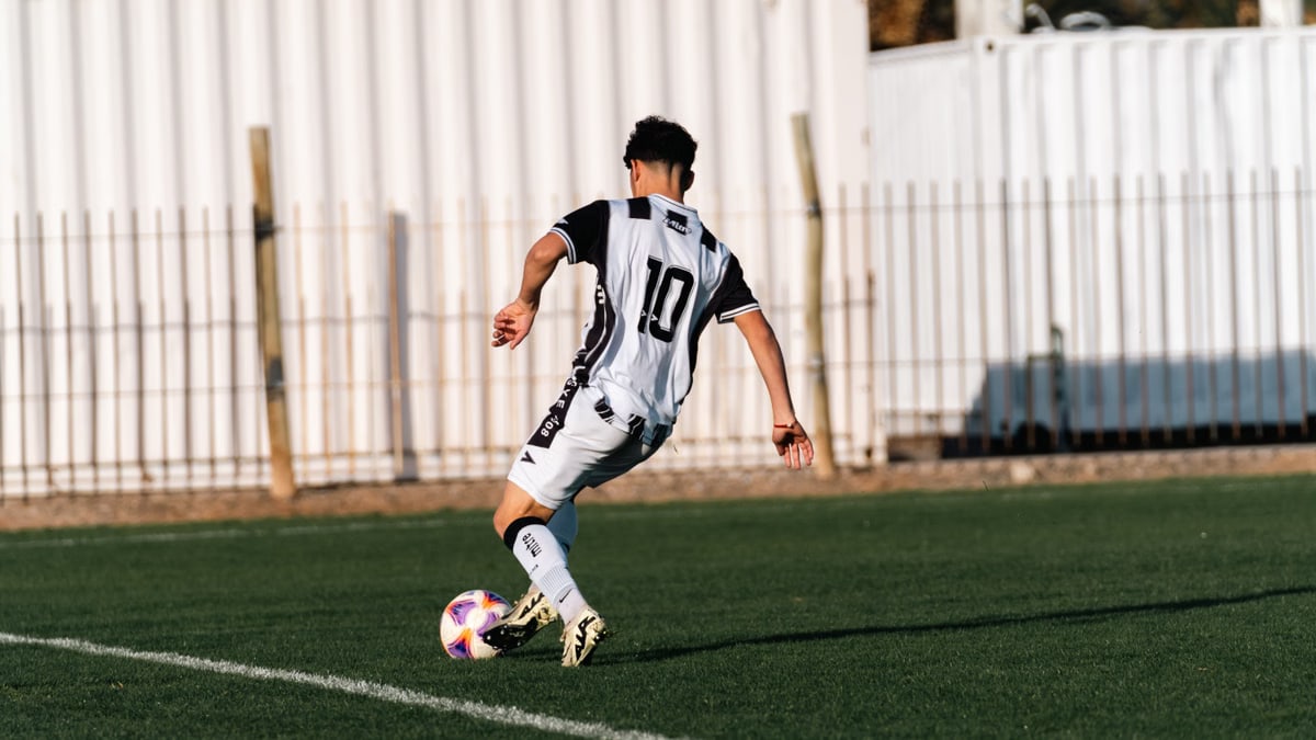 Teenage soccer player in action on outdoor sports field during day.